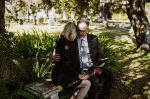 Man comforts a woman sitting on bench at cemetery