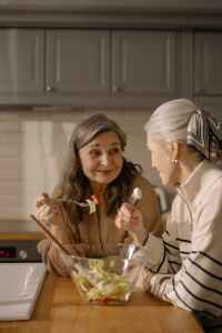 Two women share a salad in a kitchen