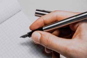 A hand holding a fountain pen over a notebook