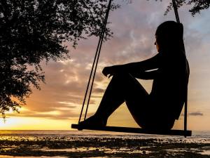 A woman sits on a swing looking at the sunset